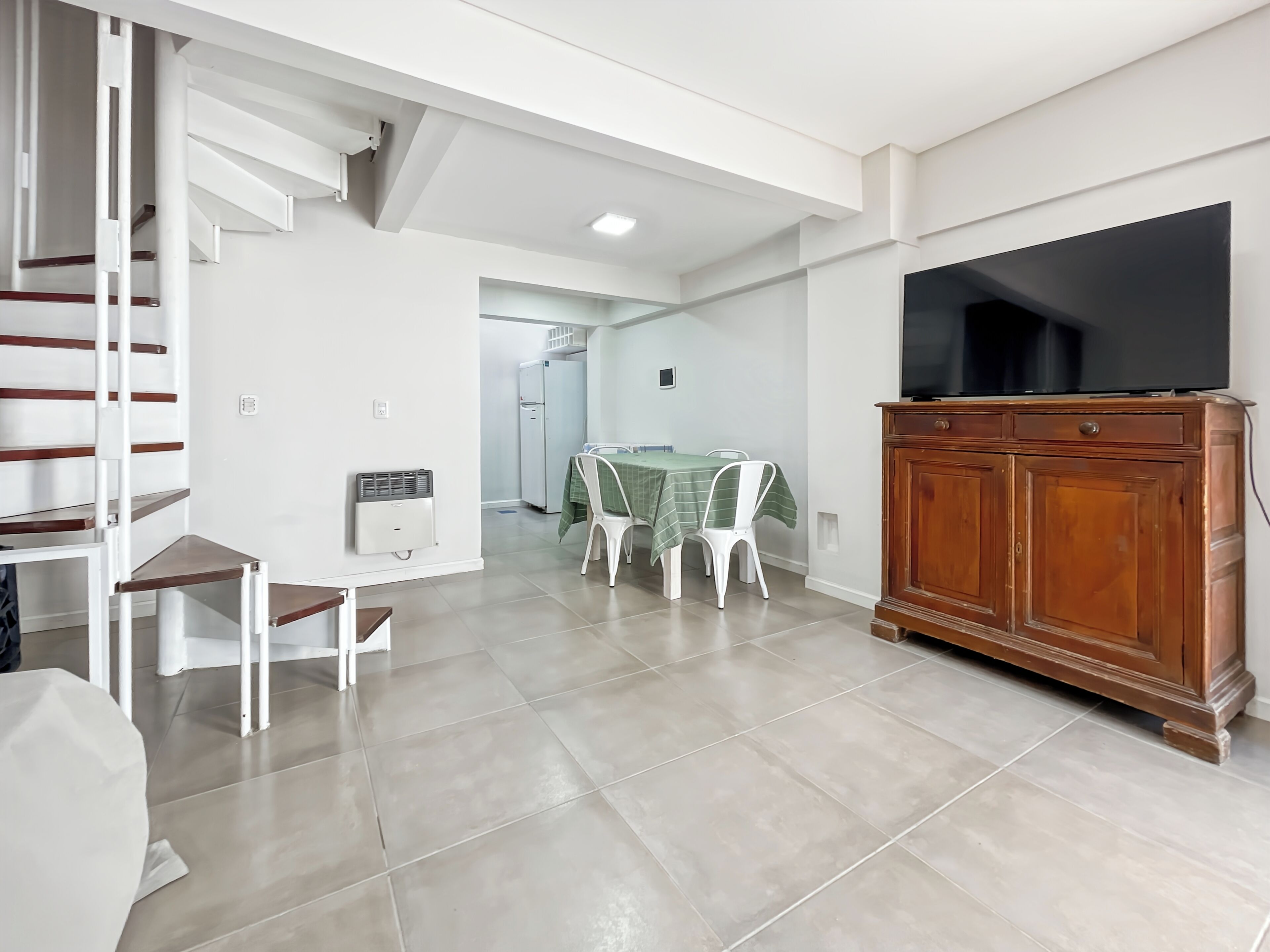 Un espacio habitable moderno con comedor, televisor y escalera.