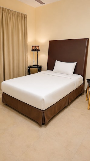 A hotel room with a large bed, a nightstand, a lamp, and a curtain. - Spacious 2-Bedroom Apartment  (Ajman)