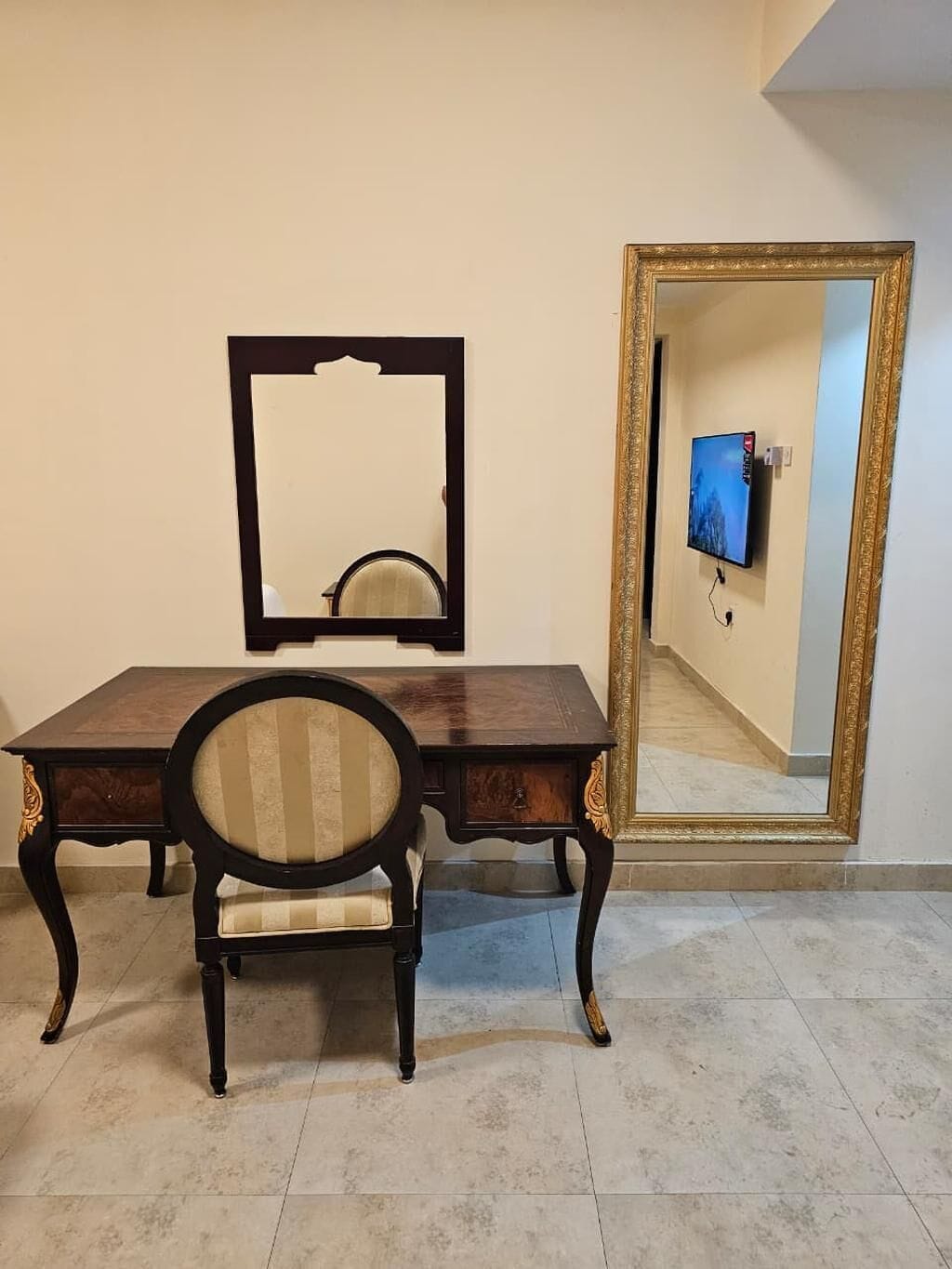 Een kamer met een houten bureau, een stoel, een spiegel en een grote spiegel aan de muur.