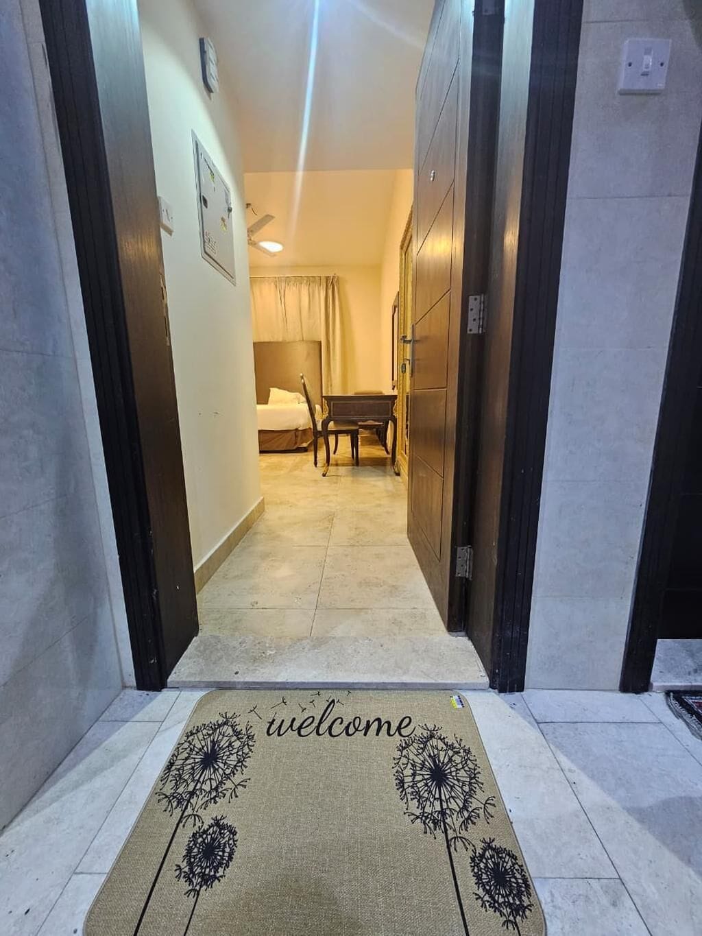 Een hotelgang met een welkomstmat, een bed, een bureau en een kledingkast.