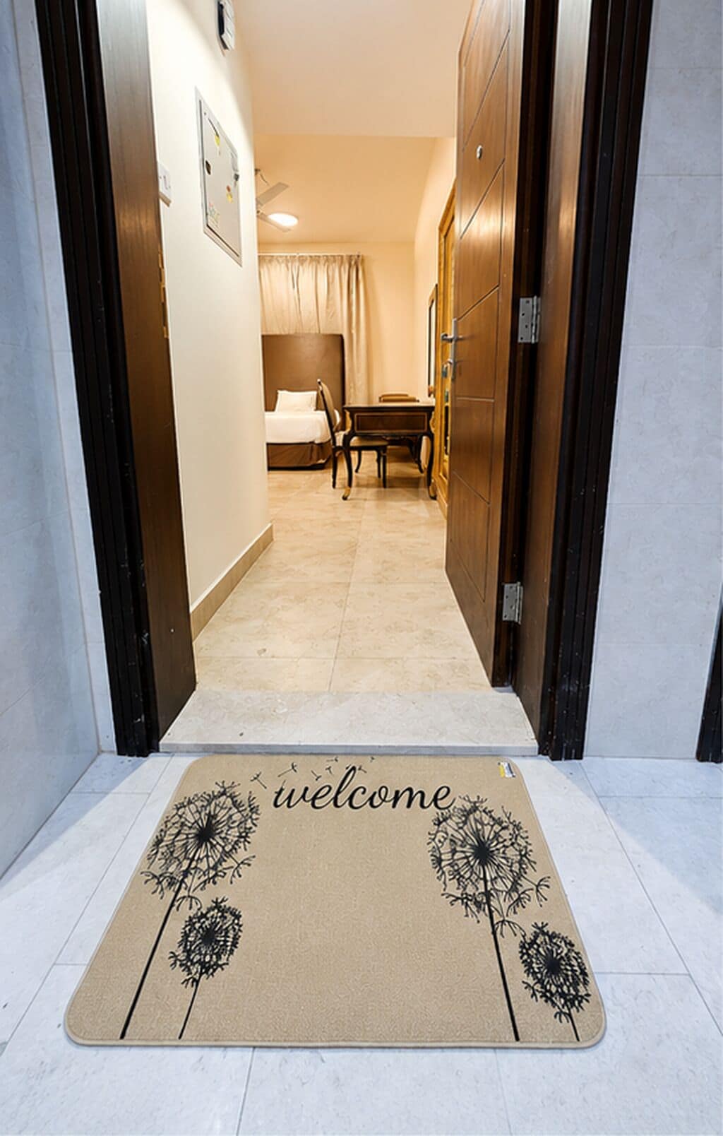 Ein Hotelflur mit Fußmatte, einem Bett, einem Tisch und einem Kleiderschrank.