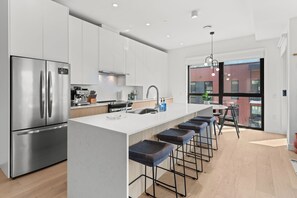 A modern kitchen with a stainless steel refrigerator, a built-in oven, and a large island with bar stools. - Rest & Roam (Revelstoke)