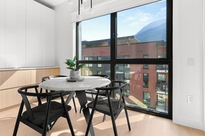 A modern room with a round table, black chairs, a potted plant, and a large window with a cityscape view. - Rest & Roam (Revelstoke)