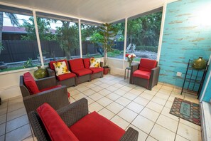 A sunlit patio with wicker furniture, a red sofa, and a small table. - Spacious 4-Bedroom Miami Home for Group Stays & Gatherings (Miami)