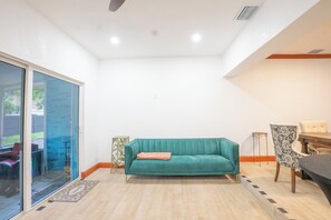 Un saló amb un sofà color turquesa, una taula de dinar, cadires i una porta corredissa de vidre que dona a una zona exterior.