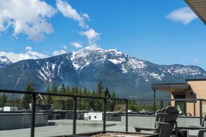 A mountain view from a balcony with a clear sky, a building with a flat roof, and a railing. - Mountain Magic (Revelstoke)