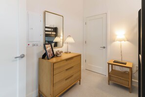 A room with a wooden dresser, a mirror, a bedside table with a lamp, and a door. - Mountain Magic (Revelstoke)