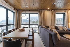 A modern interior with a wooden ceiling, large windows, a dining table, and a sofa. - Mountain Magic (Revelstoke)