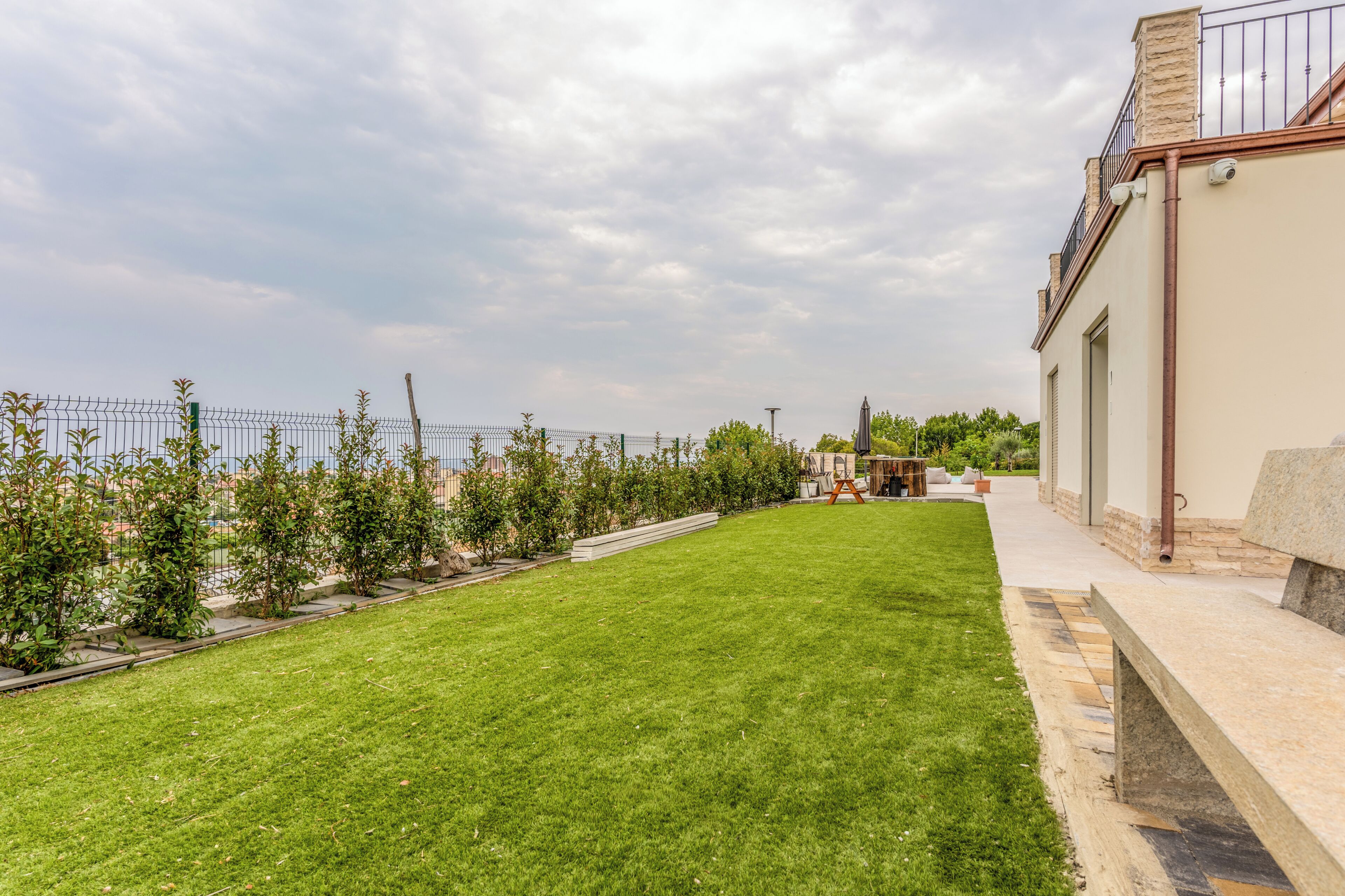 A well-maintained lawn with a metal fence, a stone pathway, and a building with a balcony.