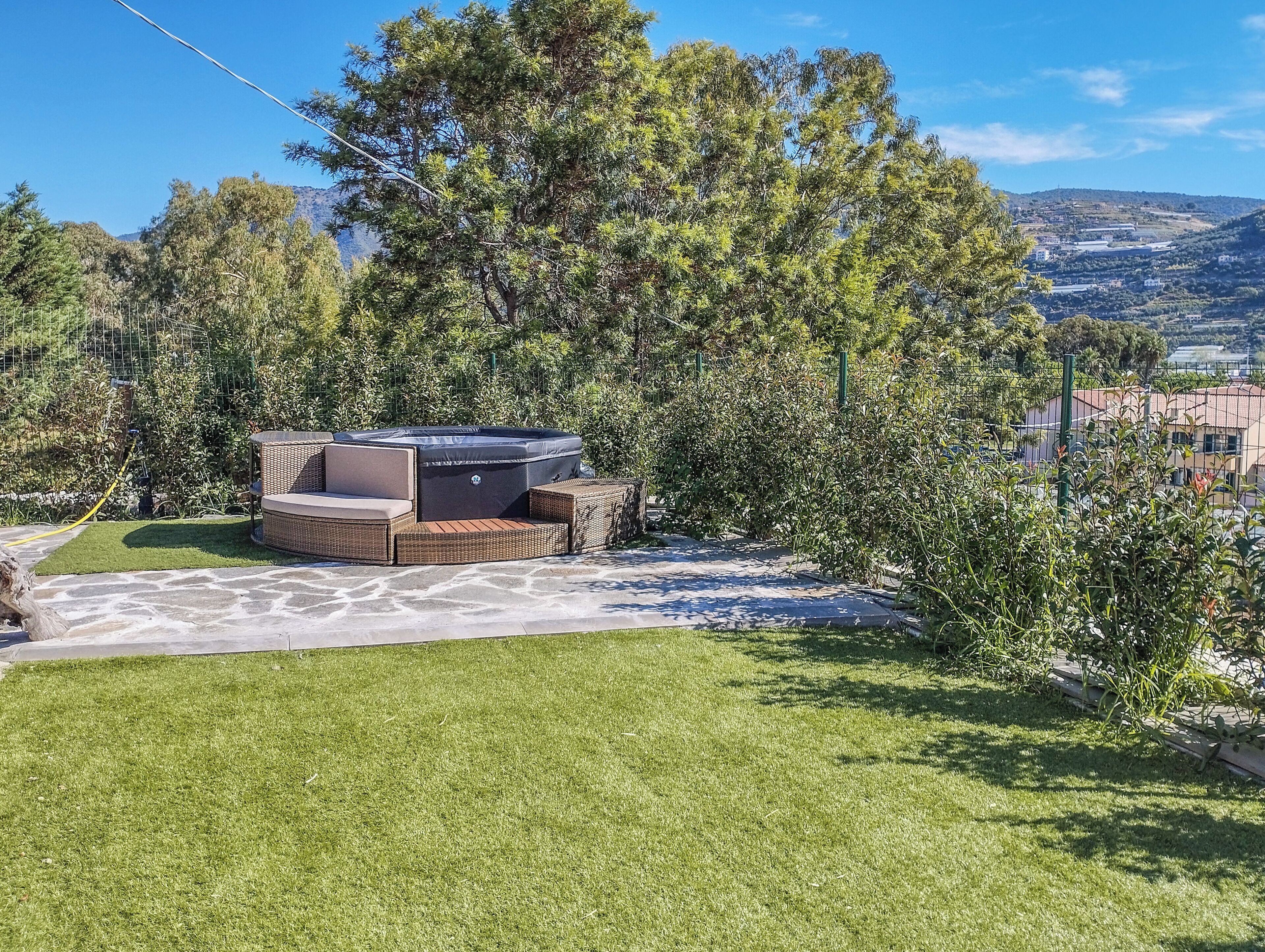 A hot tub with wicker furniture in a landscaped garden with a view of hills.