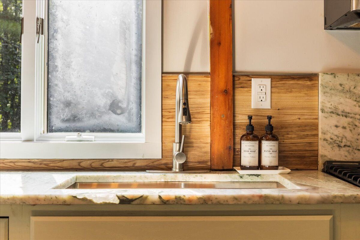 A kitchen with a window, a sink, wooden wall paneling, and two bottles of dish soap.