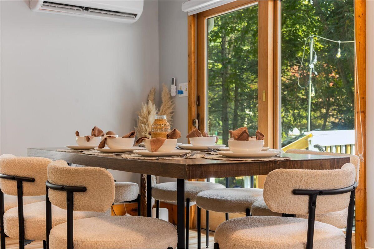 Een eetruimte met een grote tafel voor zes personen, omringd door stoelen met zwarte frames en beige kussens.