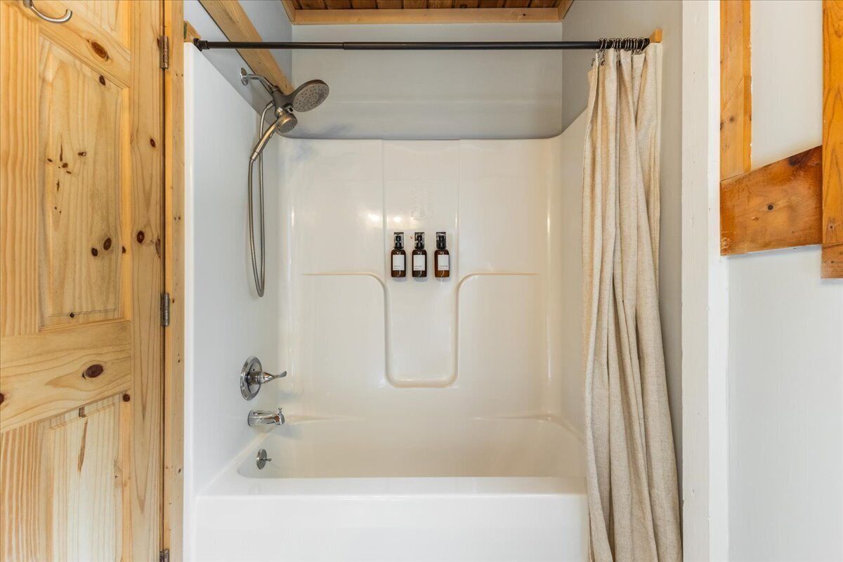 A shower with a wooden door, a showerhead, and a towel rack.