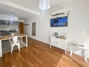 A modern kitchen with a microwave, stove, and sink. There's a dining area with a table and chairs. A TV is mounted on the wall displaying a social media app. - Charming Central Buenos Aires Apartment With City Views (Buenos Aires)