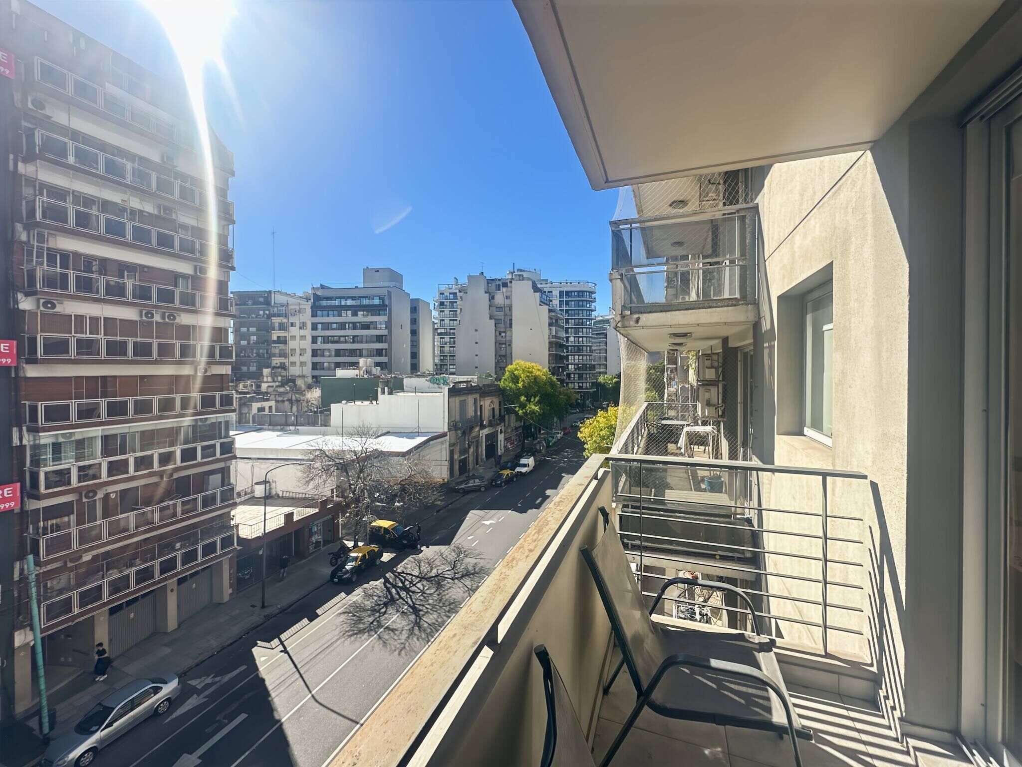 A high-rise building with multiple balconies, a clear sky, and a street view.