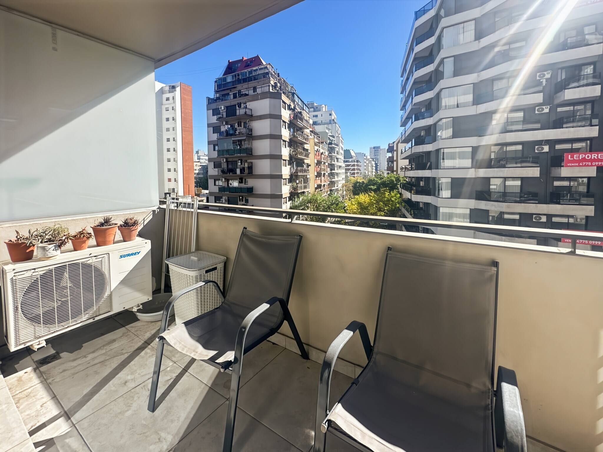 A balcony with two chairs, a white air conditioning unit, and potted plants.