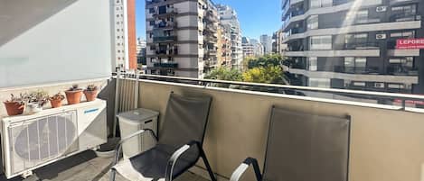 A balcony with two chairs, a white air conditioning unit, and potted plants.