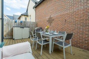 Eine Terrasse mit Esstisch und Stühlen, umgeben von einer Holzterrasse und einer Backsteinmauer.