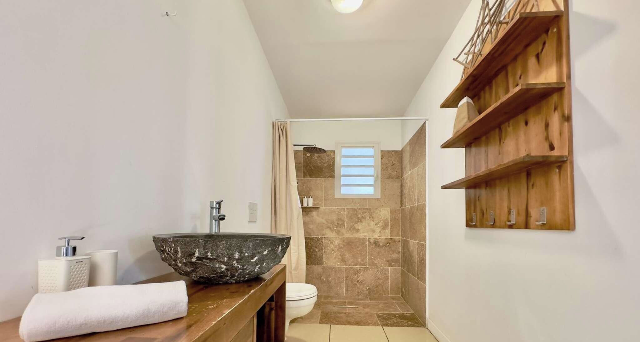 A bathroom with a stone sink, a toilet, and a shower area.