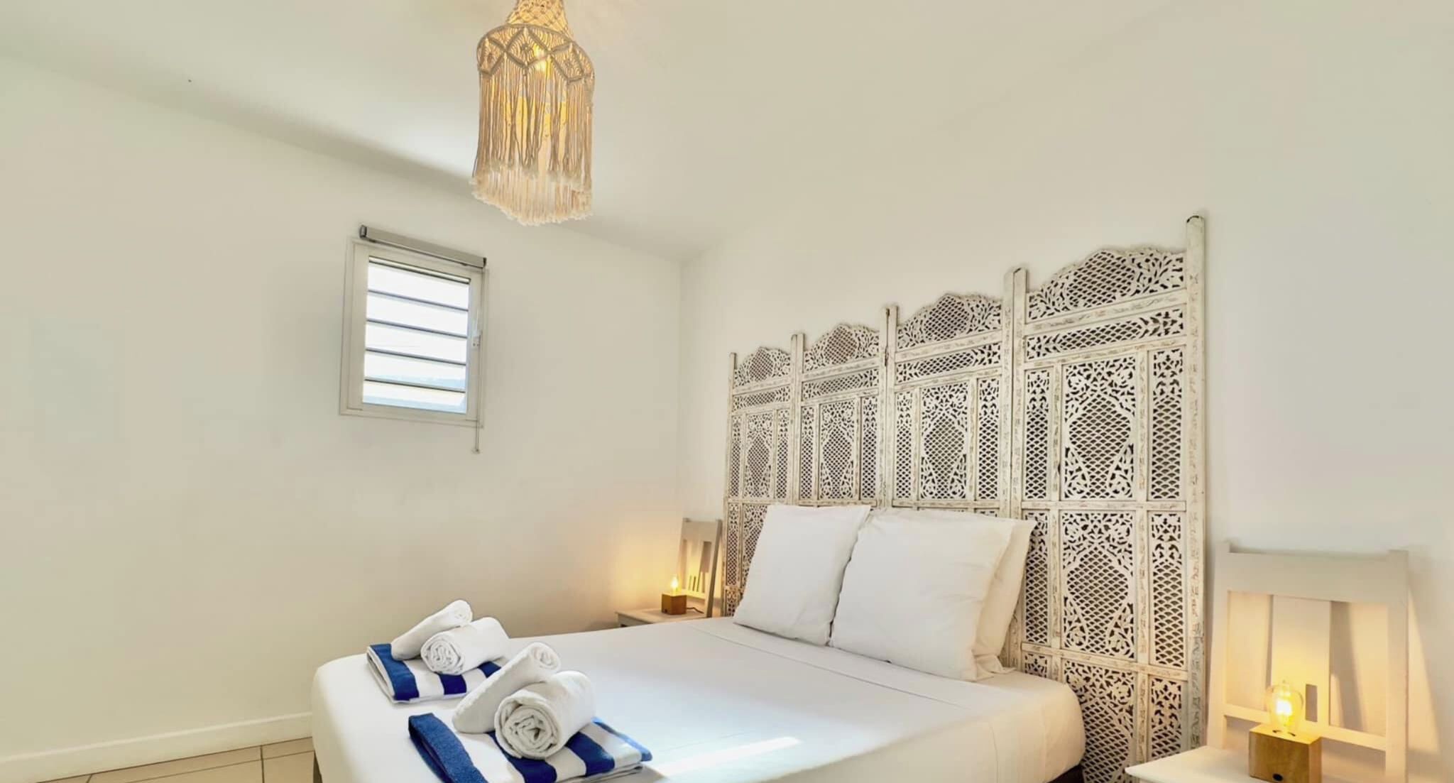 A hotel room with a bed, a decorative headboard, a small window, and a bedside lamp.