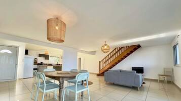 A spacious living area with a dining table, chairs, a sofa, and a staircase.