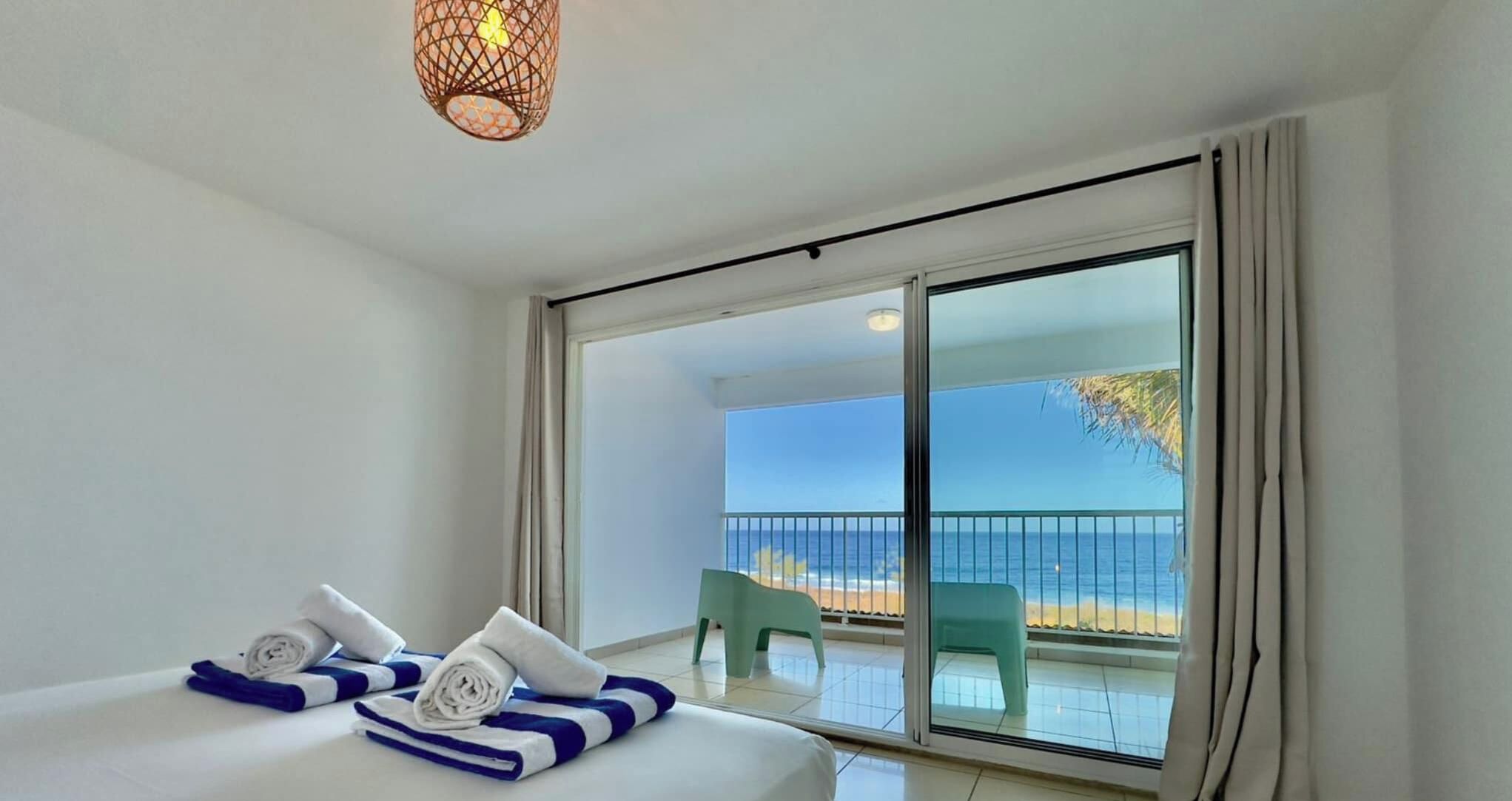 A hotel room with a bed, a view of the beach, and a balcony with a chair.