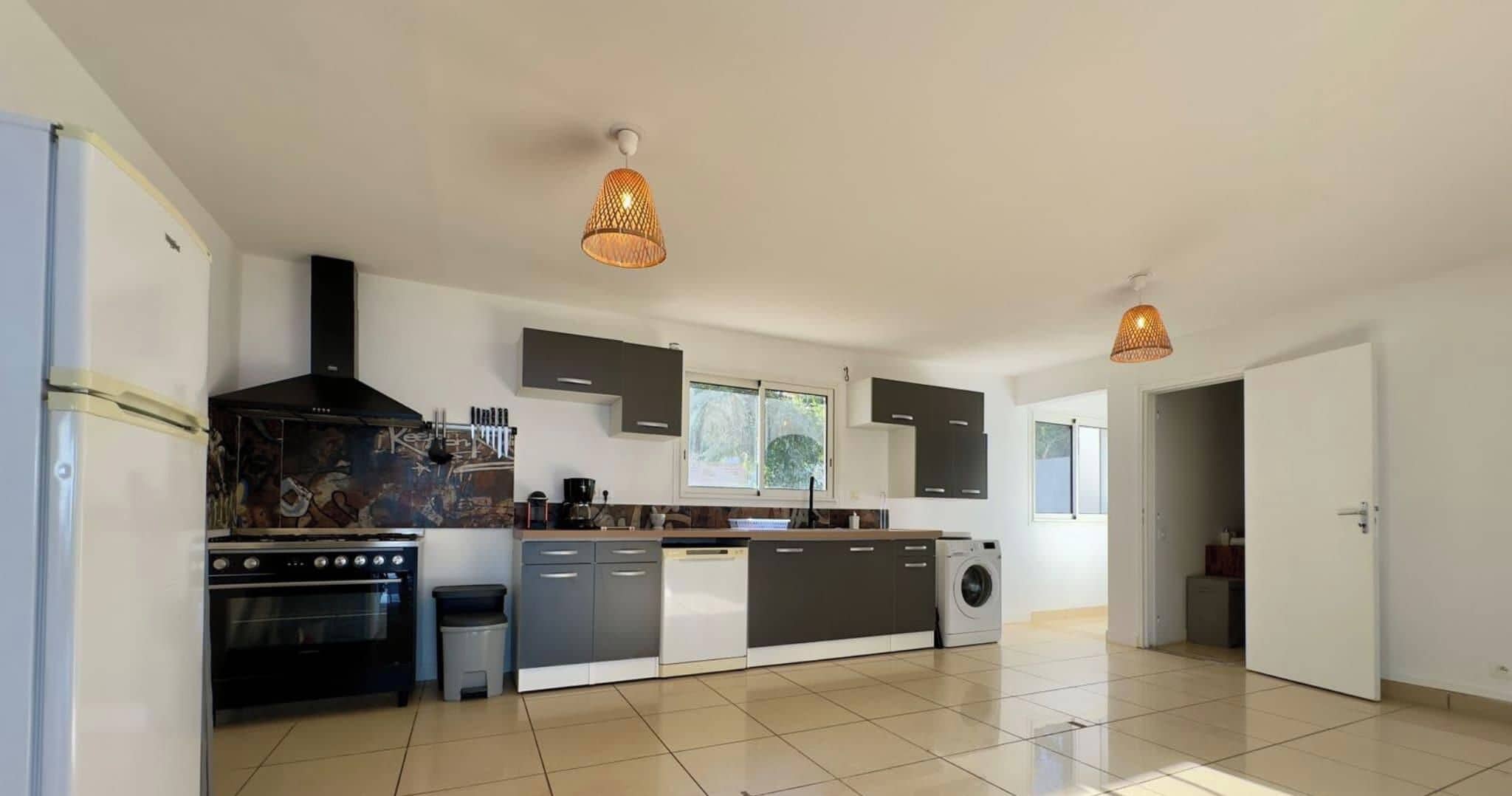 Une cuisine moderne dotée d’un îlot central, d’appareils électroménagers intégrés et de luminaires suspendus.