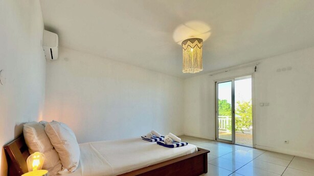 Une chambre comprenant un lit, une lampe de chevet, un luminaire au plafond et une porte-fenêtre coulissante donnant sur un espace extérieur.