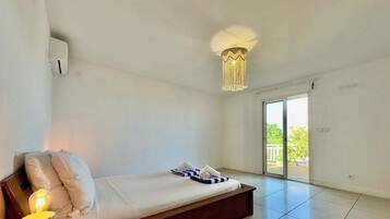 A room with a bed, a bedside lamp, a ceiling light fixture, and a sliding glass door leading to an outdoor area.