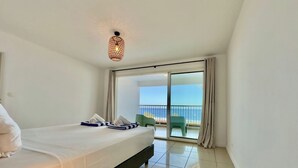 Une chambre d’hôtel avec un lit, un balcon donnant sur la mer et un luminaire au plafond.