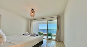 A hotel room with a bed, a balcony with a view of the sea, and a ceiling light fixture. - Whale Beach Villa by HILO Collection (Les Trois-Bassins)