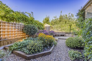Un jardí amb una tanca de fusta, una caseta de fusta i diverses plantes i flors.