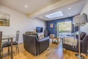 A modern living room with a sofa, a dining table, and a TV. - Charming House with Pretty Garden & Parking - Pass the Keys (Chichester)