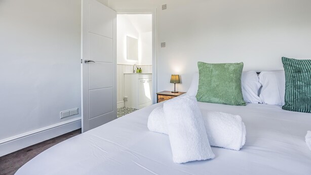 A hotel room with a bed, pillows, a nightstand, a lamp, and a bathroom visible through an open door. - Lovely 2 Bedroom Coastal Flat - Pass the Keys (Bognor Regis)