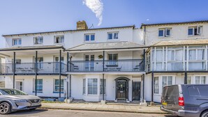 A row of white two-story buildings with balconies, a parked car, and a clear sky. - Lovely 2 Bedroom Coastal Flat - Pass the Keys (Bognor Regis)