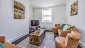 A living room with a TV, wooden coffee table, leather sofas, and artwork on the walls. - Lovely 2 Bedroom Coastal Flat - Pass the Keys (Bognor Regis)