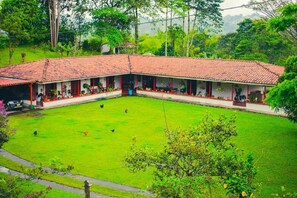 A two-story building with a red-tiled roof, a covered courtyard, and a lush green lawn. - Villa Cristina - Casa Boutique (PEREIRA)