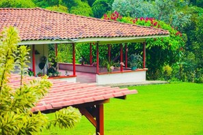 A covered outdoor area with a tiled roof, surrounded by lush greenery and flowering plants. - Villa Cristina - Casa Boutique (PEREIRA)