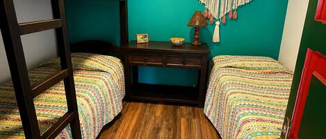 Una habitación con dos literas, un escritorio, un tapiz de macramé y suelo de madera.