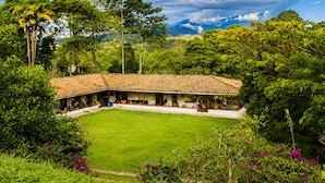 Un edificio espacioso con techo de tejas y un patio central rodeado de abundante vegetación y árboles.