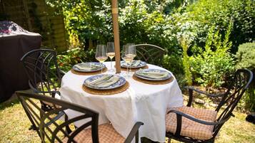 An outdoor dining area with a round table set for four, surrounded by chairs with cushions.