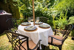 An outdoor dining area with a round table set for four, surrounded by chairs with cushions. - Stone Cottage Sleeps 4 with Fireplace · Walk to Rodborough Common (Gloucestershire)