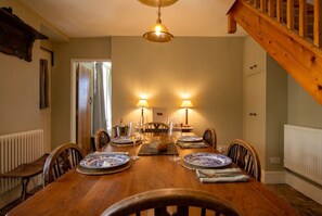 Een eetkamer met een houten tafel voor vier personen, met aan weerszijden lampen, een radiator en een trap.