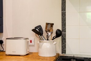 A kitchen with a white toaster on the counter, a white ceramic pot with utensils, and a tiled backsplash. - Stone Cottage Sleeps 4 with Fireplace · Walk to Rodborough Common (Gloucestershire)