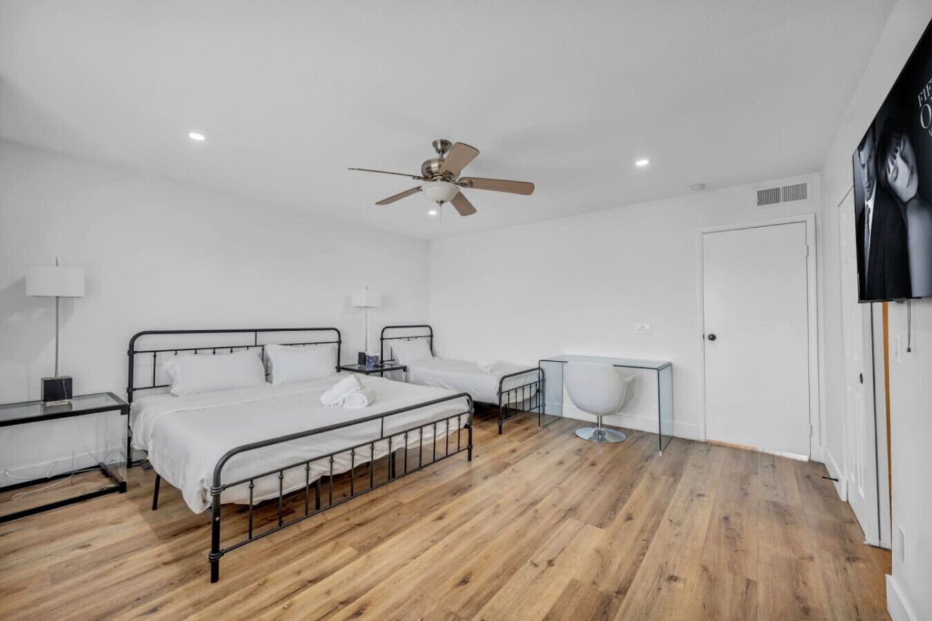 Une chambre à coucher comprenant un lit, des tables de chevet, un ventilateur de plafond et une petite table avec une chaise.