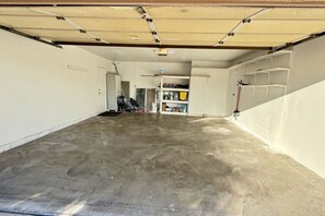 Ett garage med ett betonggolv, vita väggar och en delvis öppen dörr som leder in till ett rum med hyllor och verktyg.
