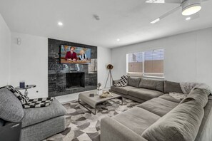 A living room with a fireplace, a sofa, a coffee table, and a television. - Modern Home By The Strip (Las Vegas)