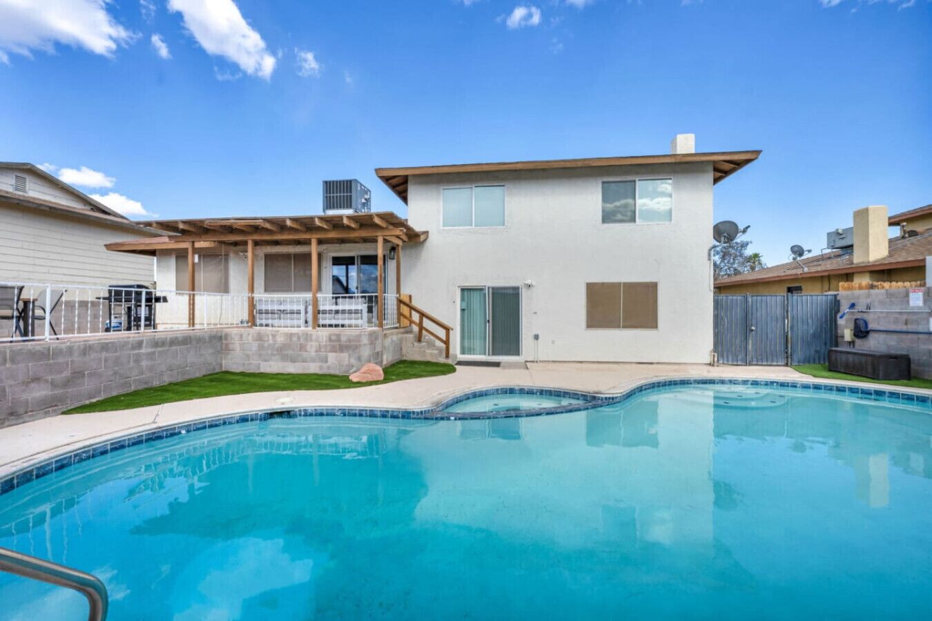 A residential property with a swimming pool, a covered patio, and a two-story house.
