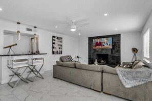 A modern living room with a sectional sofa, a fireplace, a television mounted above it, and a desk with a telescope. - Modern Home By The Strip (Las Vegas)
