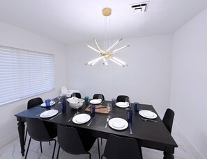 A dining area with a black table set for four, white plates, blue glasses, and a central light fixture. - Modern Home By The Strip (Las Vegas)